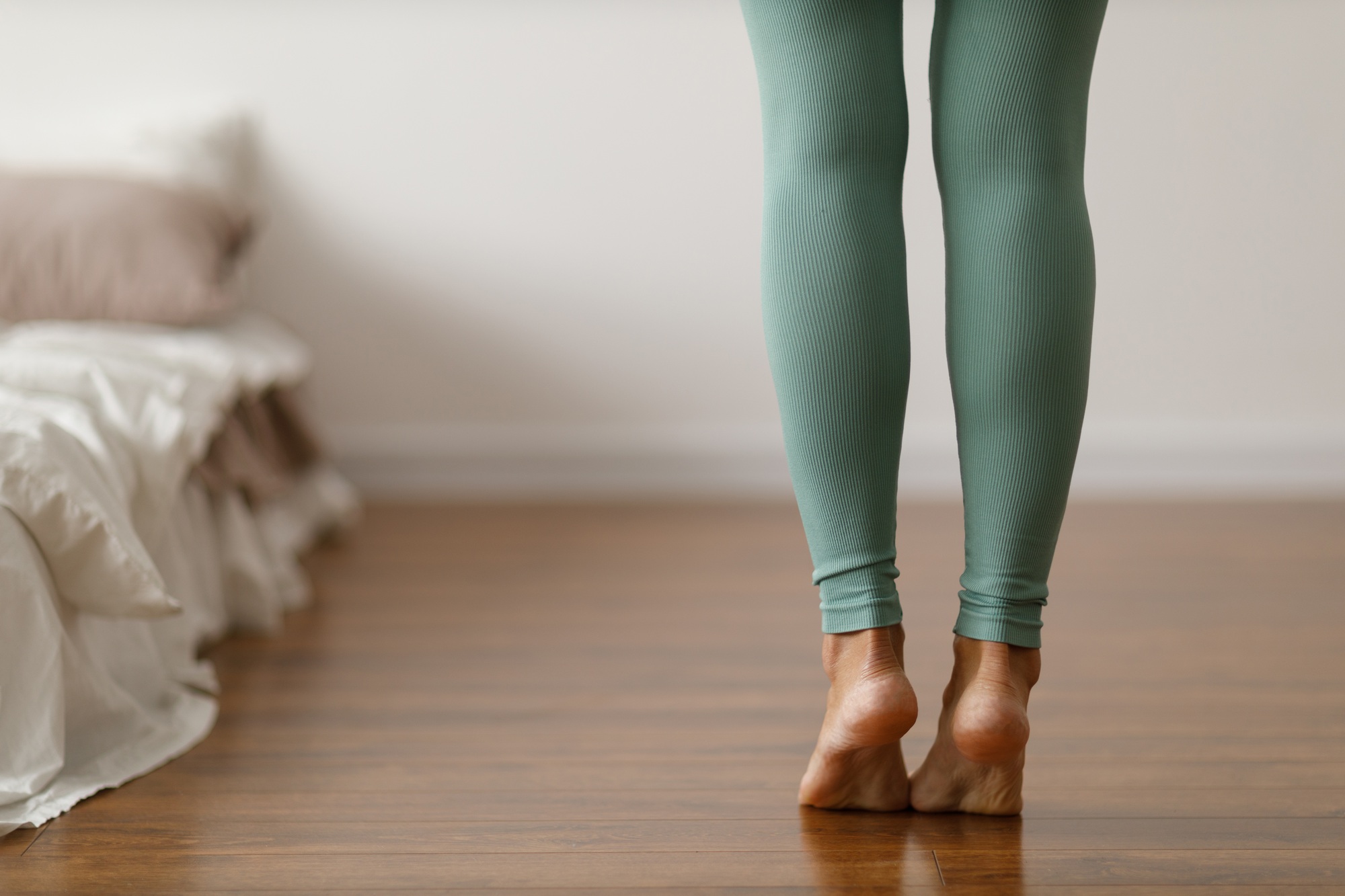 Young woman in sports leggings walks barefoot on the warm floor in the bedroom.